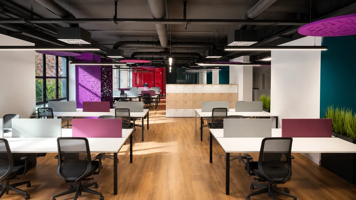 Open space con soffitto tecnico a vista, postazioni chiare e partizioni magenta