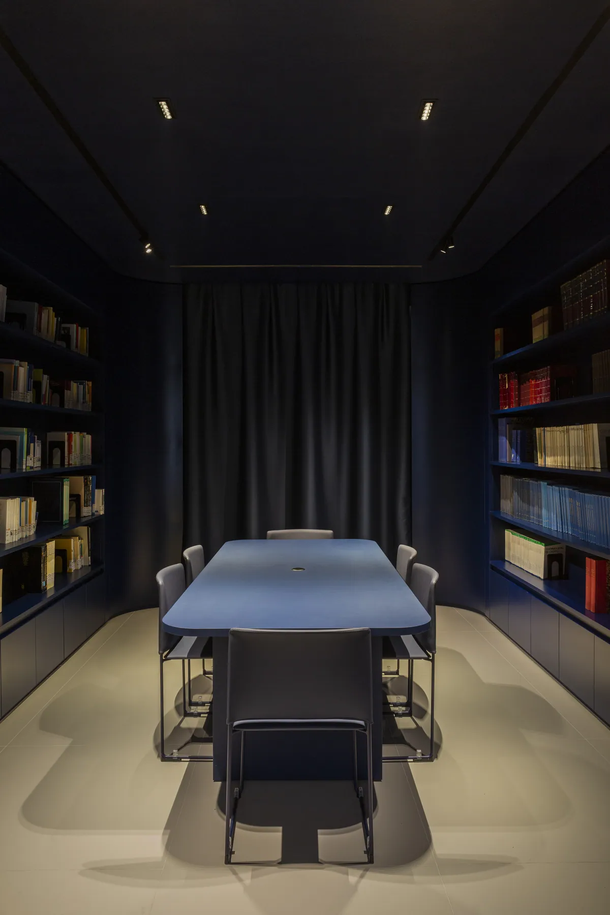 Sala riunioni scura con libreria a parete, tavolo blu e illuminazione puntuale