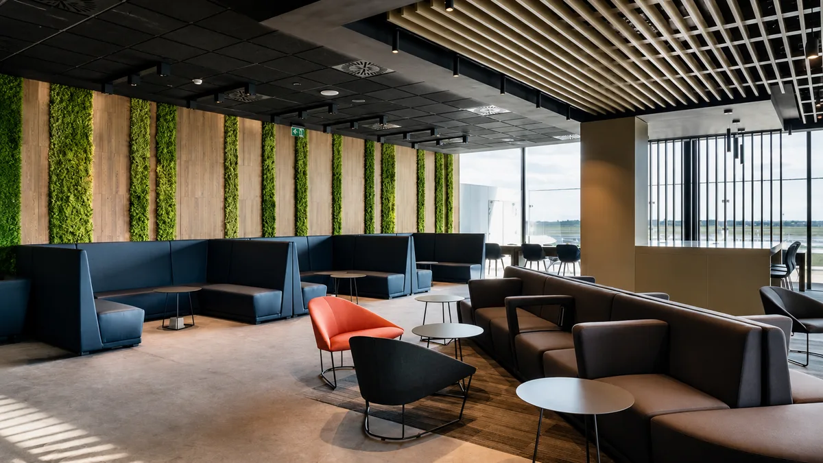 Area lounge con divani blu e grigi, poltroncine arancio e parete verticale vegetale