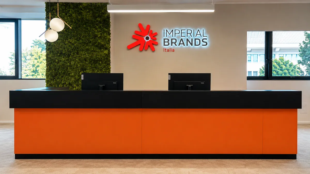 Reception con bancone arancio, parete in verde stabilizzato e insegna Imperial Brands