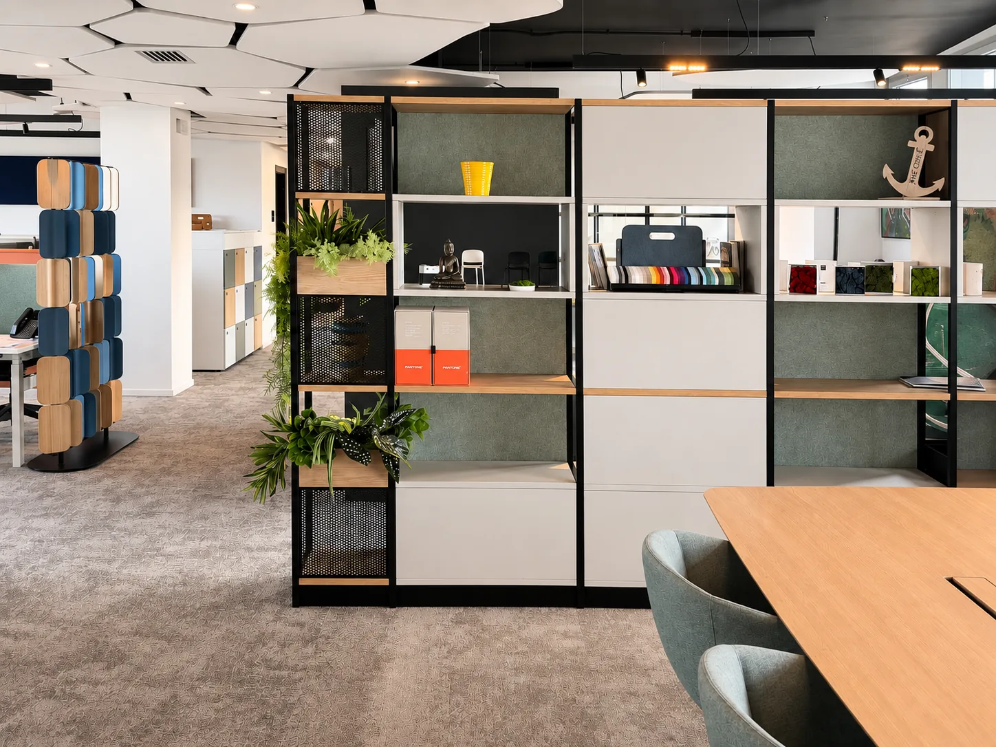 Parete espositiva del Workplace Lab con campioni di finiture, tessuti e accessori accanto a un tavolo riunioni