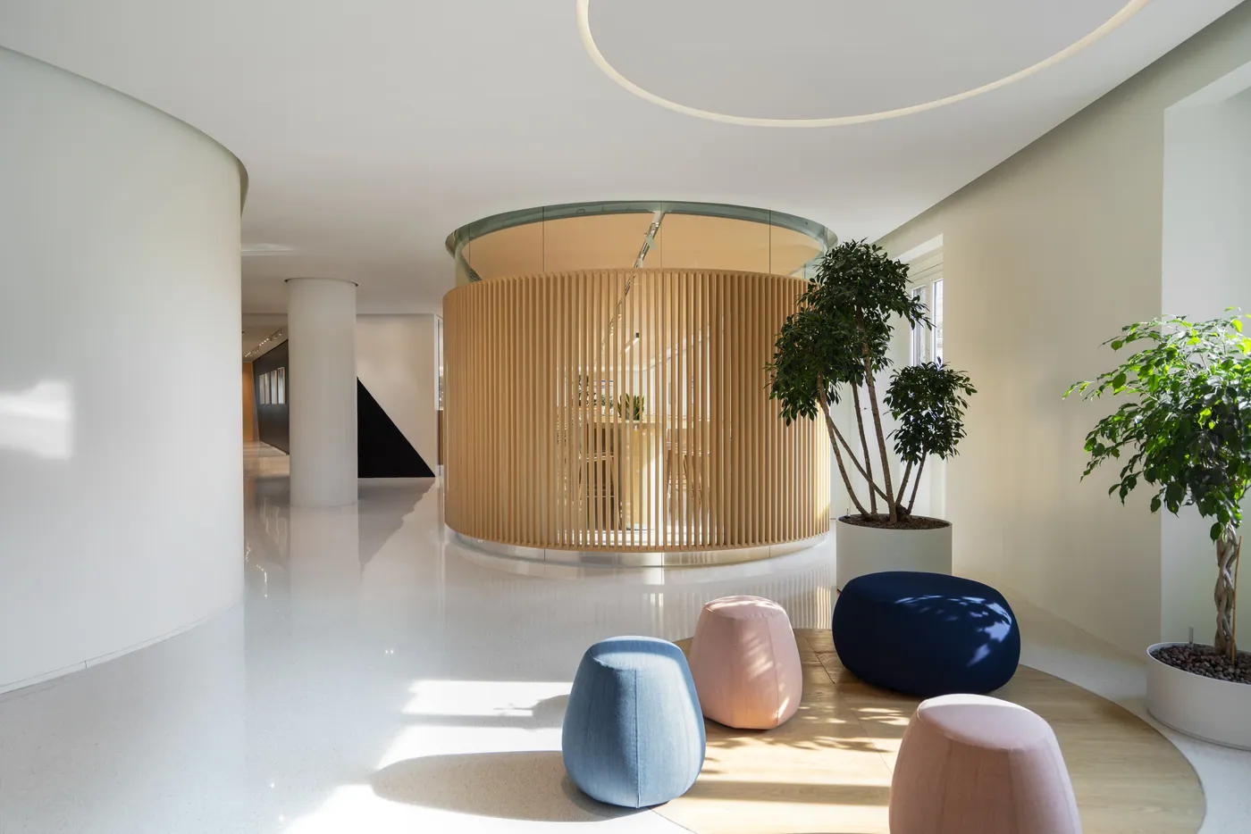 Area lounge con volume cilindrico in legno, pouf colorati e piante