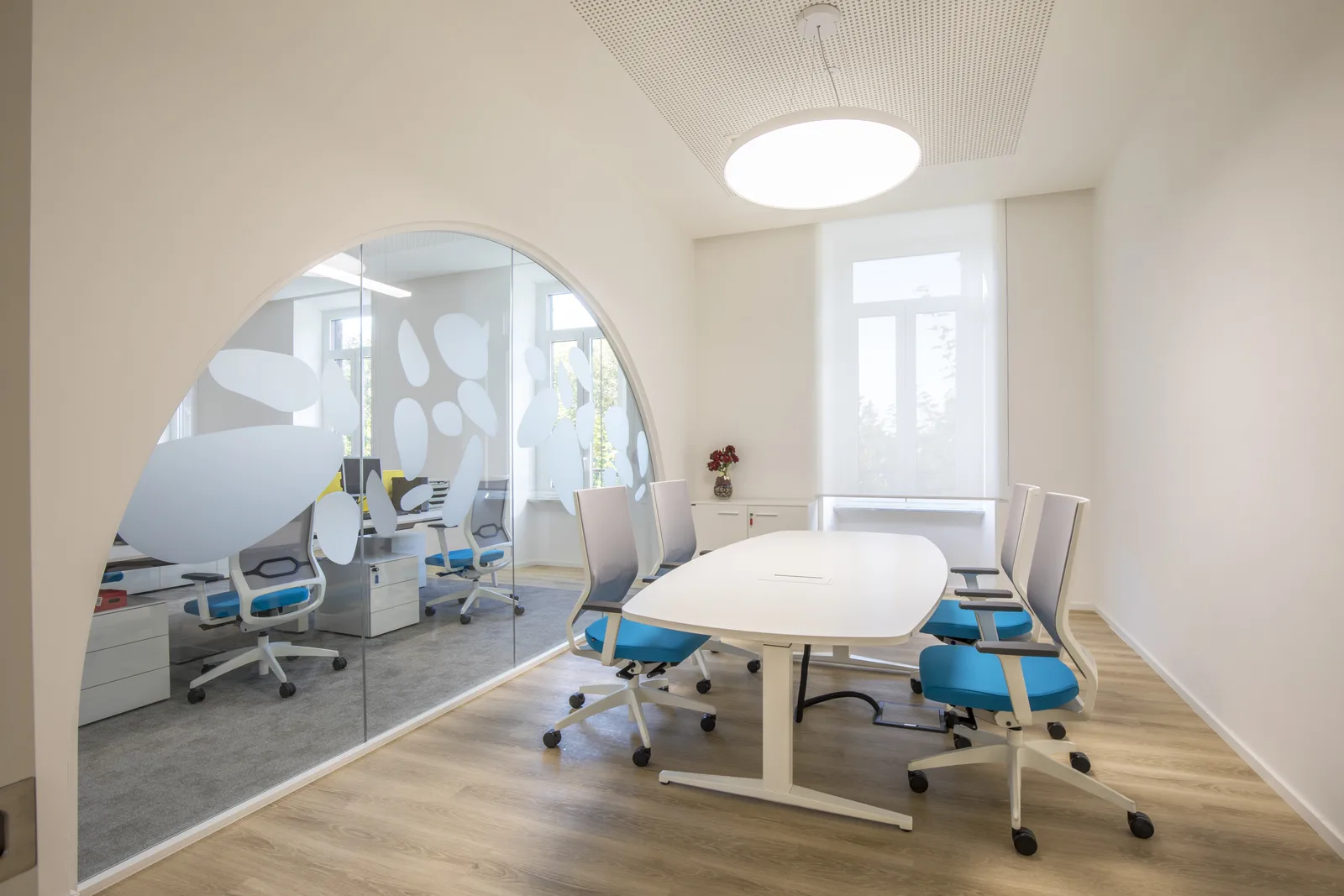 Sala riunioni con tavolo bianco, sedute azzurre e parete vetrata ad arco decorata