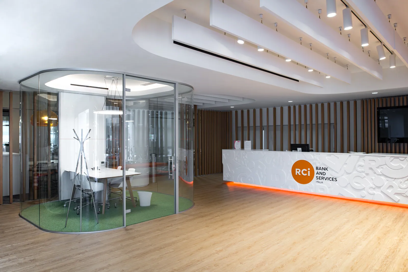Reception RCI con bancone bianco curvo, parete a doghe in legno e partizioni vetrate curve